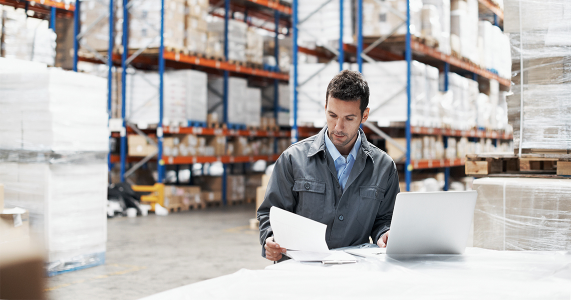 A man stands in a warehouse looking at paperwork.