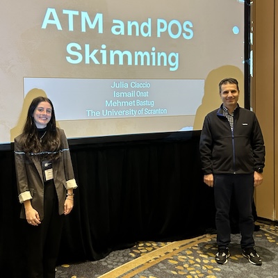 A woman and man stand in front of a projector screen in an auditorium.